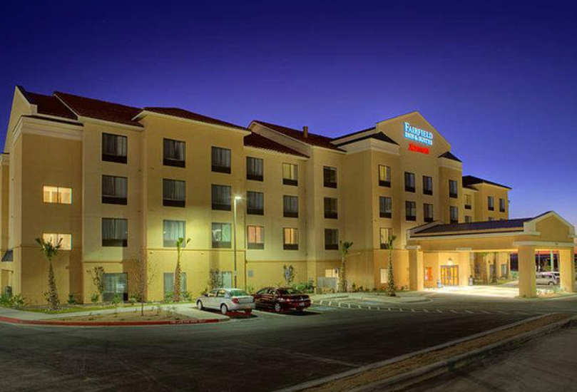 Fairfield Inn by Marriott hotel at night. Exterior view, beige building, lit entrance, parked cars.