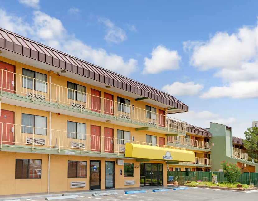 Exterior of a yellow motel with a brown awning and blue sky.