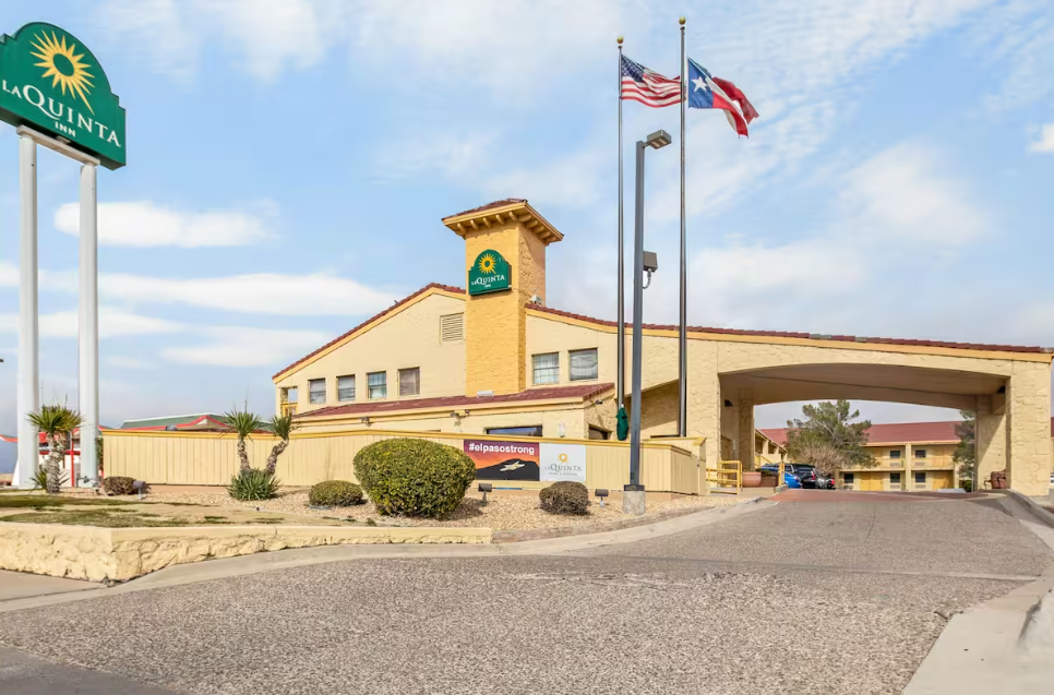 La Quinta Inn building with a road leading to the entrance, flags, and a sign against a blue sky.