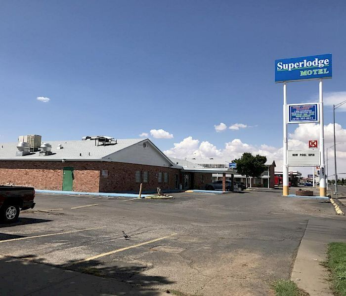 Superlodge Motel exterior with a brown brick building, blue sign, and parking lot on a sunny day.