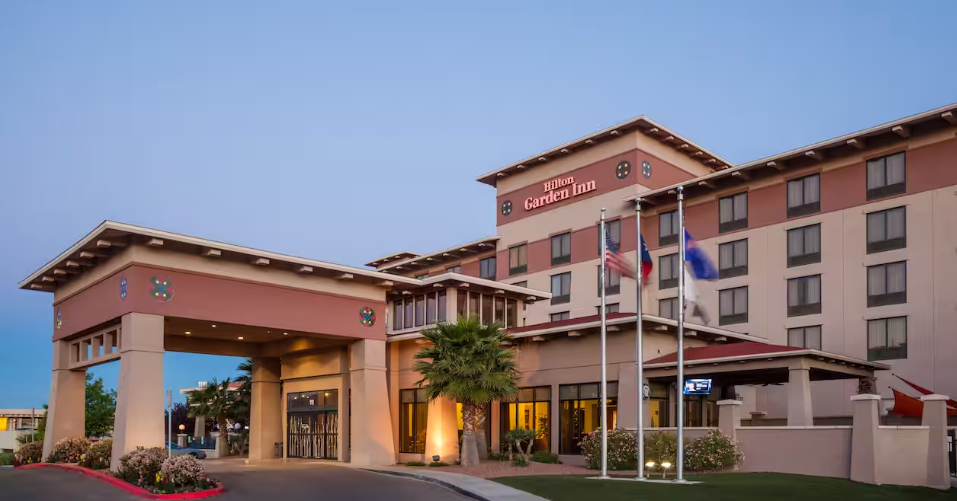 Hotel exterior with a stucco facade, flags, and entrance.