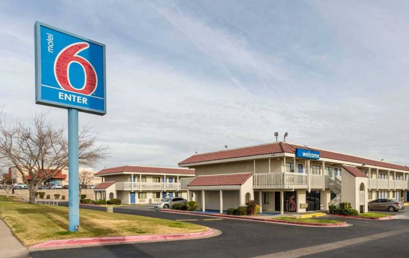 Motel 6 exterior with blue sign, beige buildings, and a parking lot. Sunny daytime.