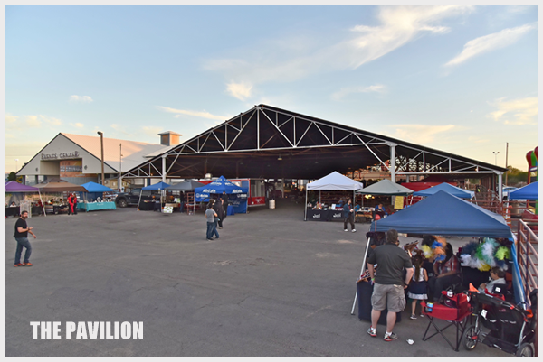 Pavilion hosting an outdoor market with vendors and shoppers on a sunny day.