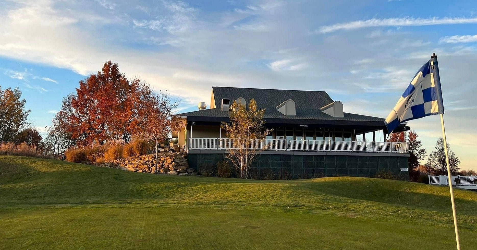 Golf course clubhouse with a checkered flag, fall foliage, and a blue sky.