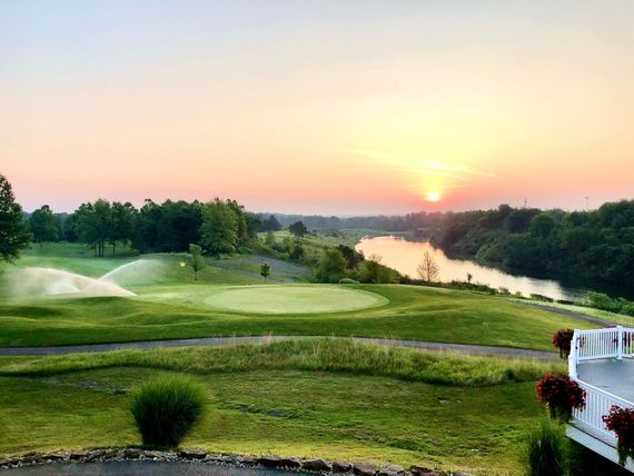 Aerial view of a green golf course with sand traps and houses in the background under a blue sky.