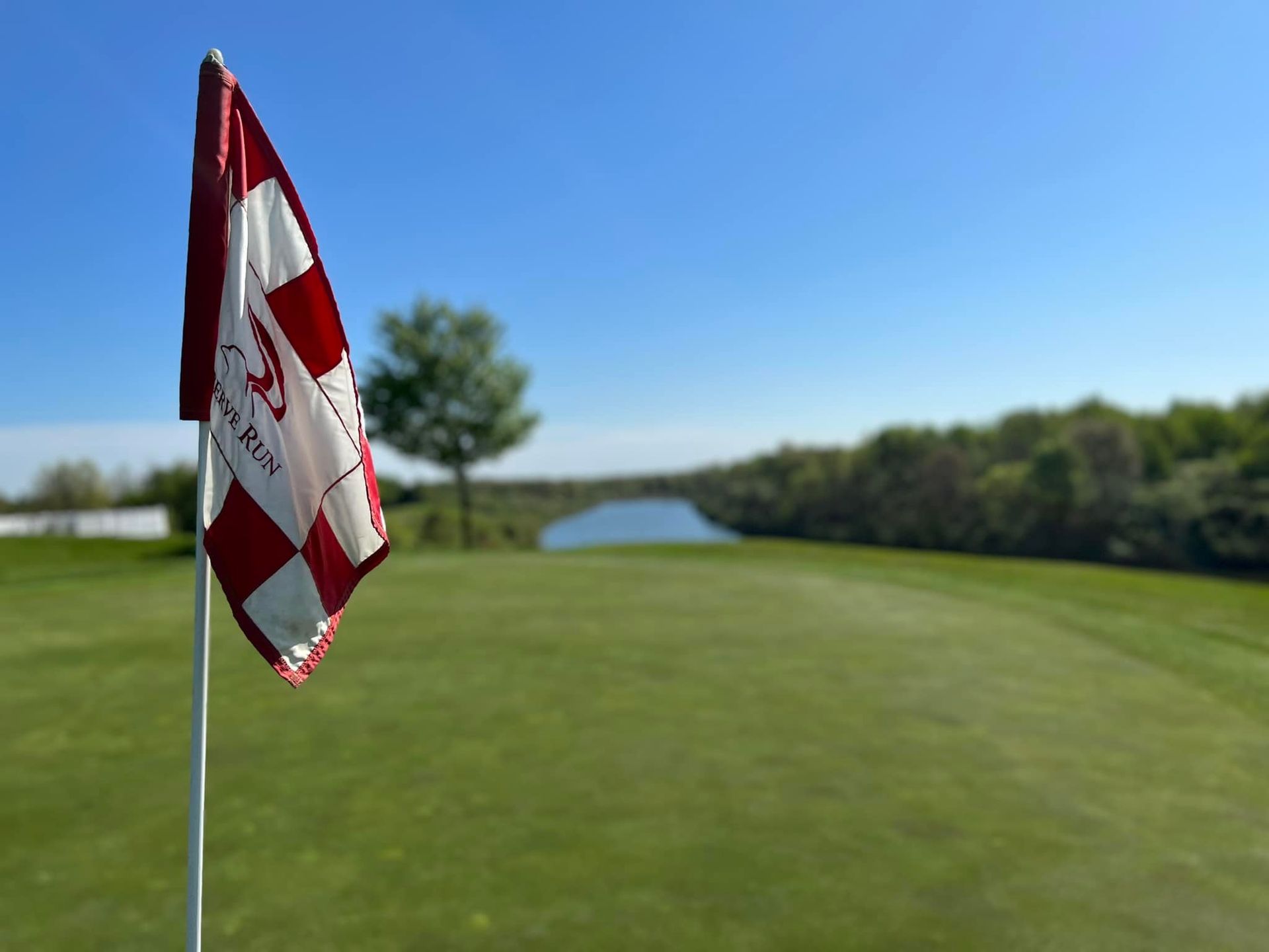 Golf course scene with sand trap, green grass, and trees under a blue sky.