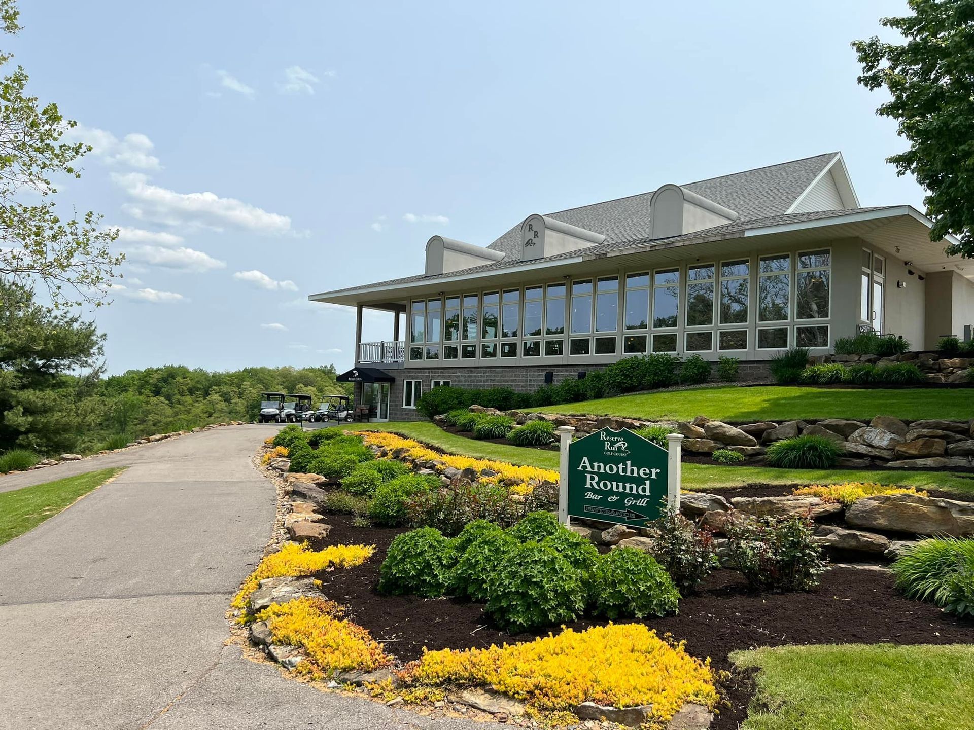 Restaurant interior with tables, chairs, bar, and multiple TVs. Black chairs, wooden tables, and a long bar.