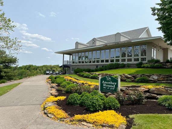 Restaurant interior with tables, chairs, bar, and multiple TVs. Black chairs, wooden tables, and a long bar.