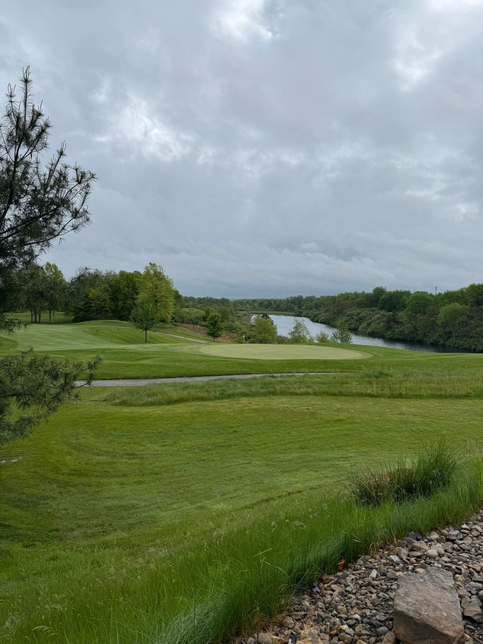 Green golf course overlooking a lake under a cloudy sky.
