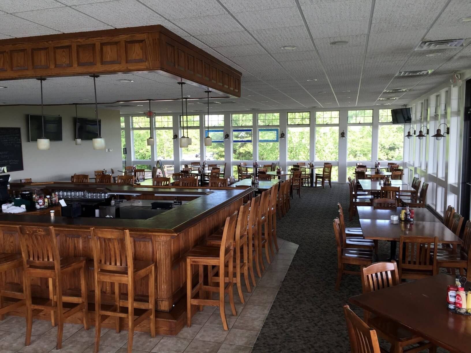 Interior of a restaurant/bar with wooden bar stools, tables, and large windows.