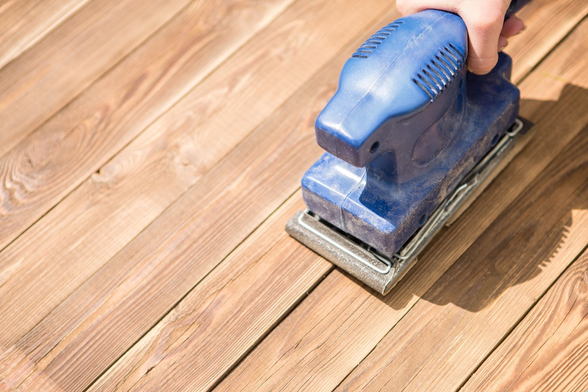 A person is sanding a wooden surface with a sander.