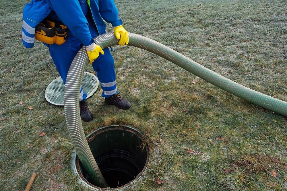 A man is pumping water into a septic tank with a hose.