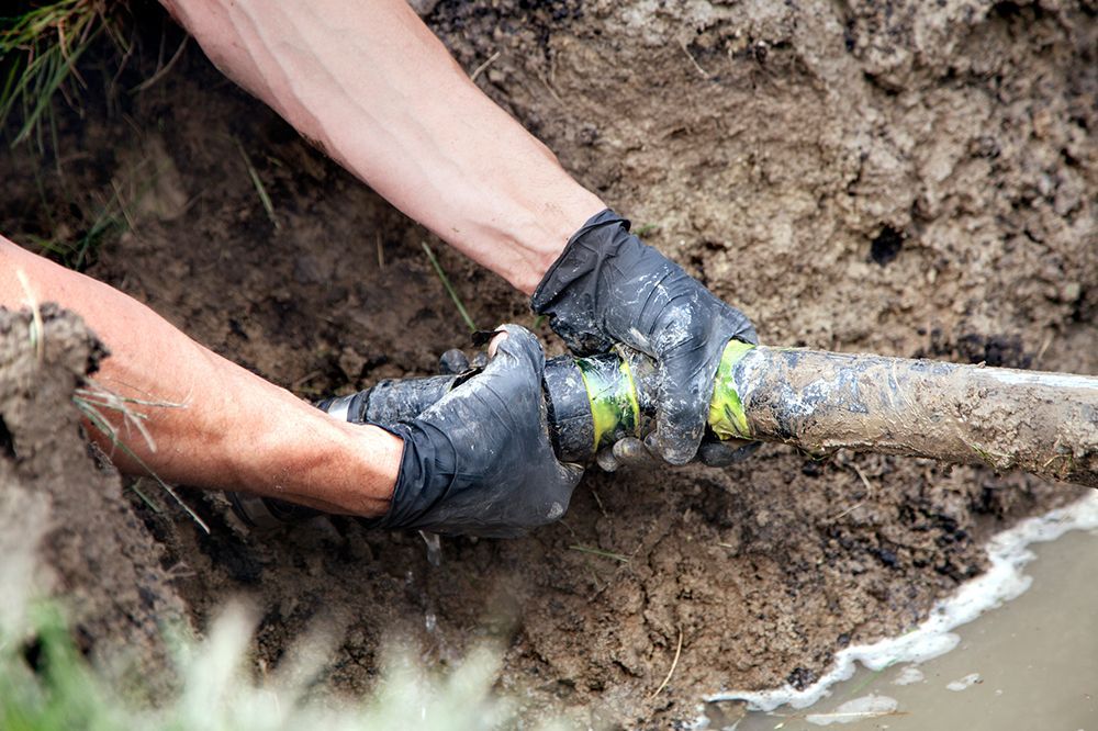 A man is fixing a pipe in the mud.