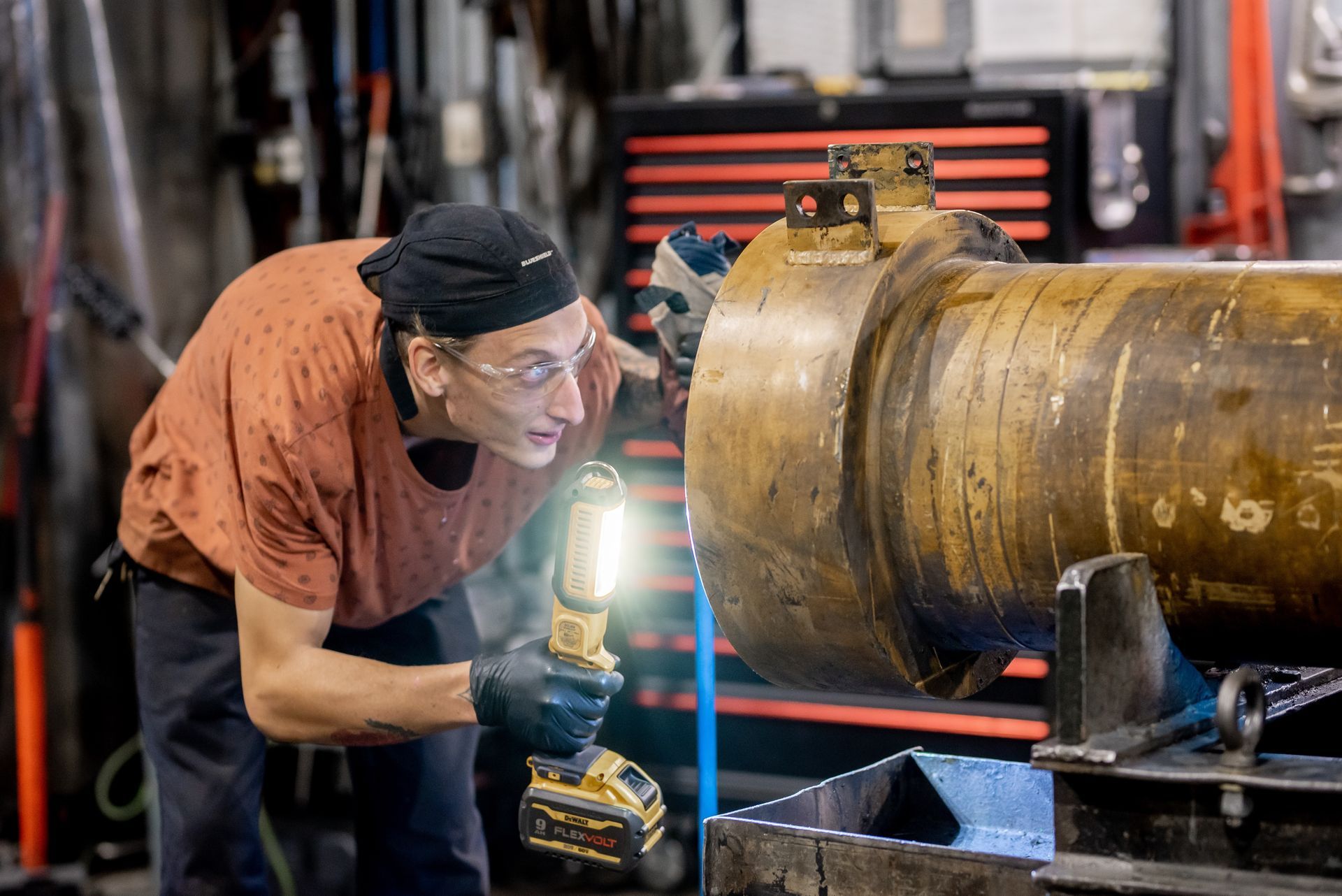Mechanic inspecting large metal cylinder with flashlight in workshop.