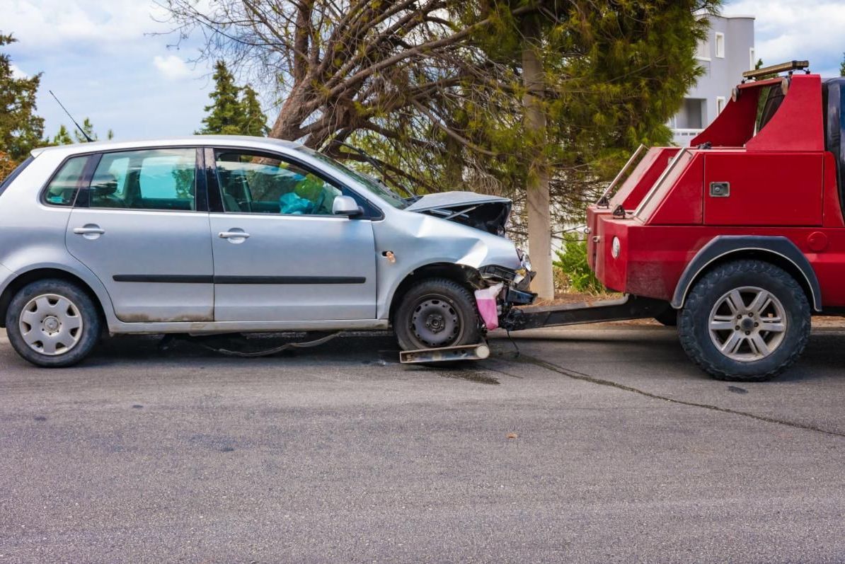 A Tow Truck is Towing a Damaged Car on the Side of the Road — DJ's Tilt Tray Service in Coffs Harbour, NSW