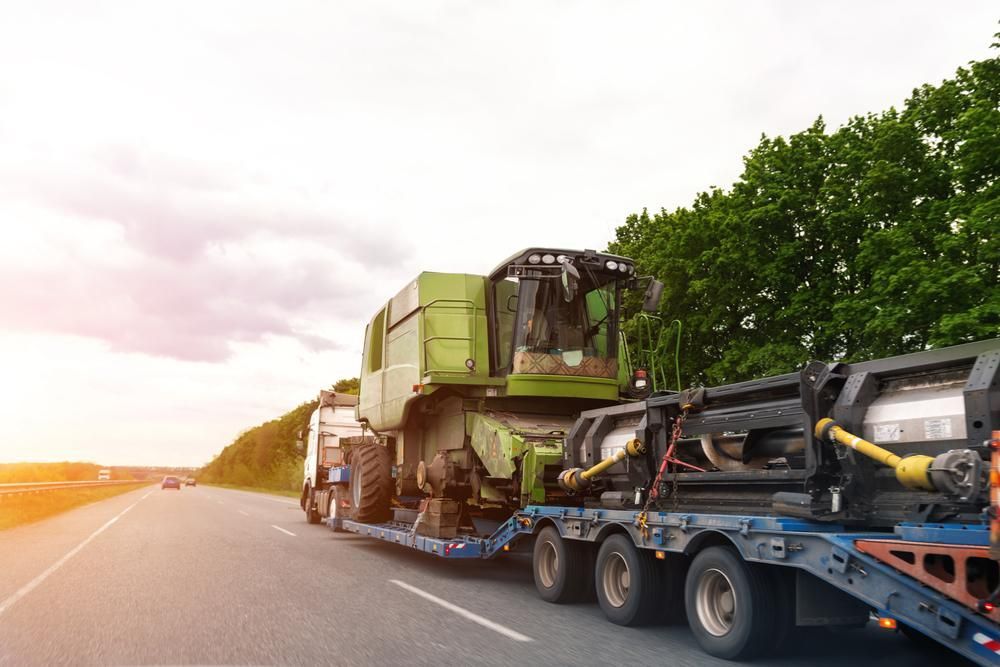 A Semi Truck is Carrying a Combine Harvester Down a Highway — DJ's Tilt Tray Service in Coffs Harbour, NSW