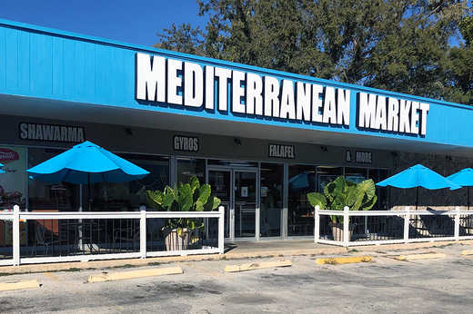 a blue building with a sign that says `` mediterranean market '' and blue umbrellas in front of it .