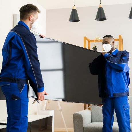 two men wearing masks are carrying a flat screen tv