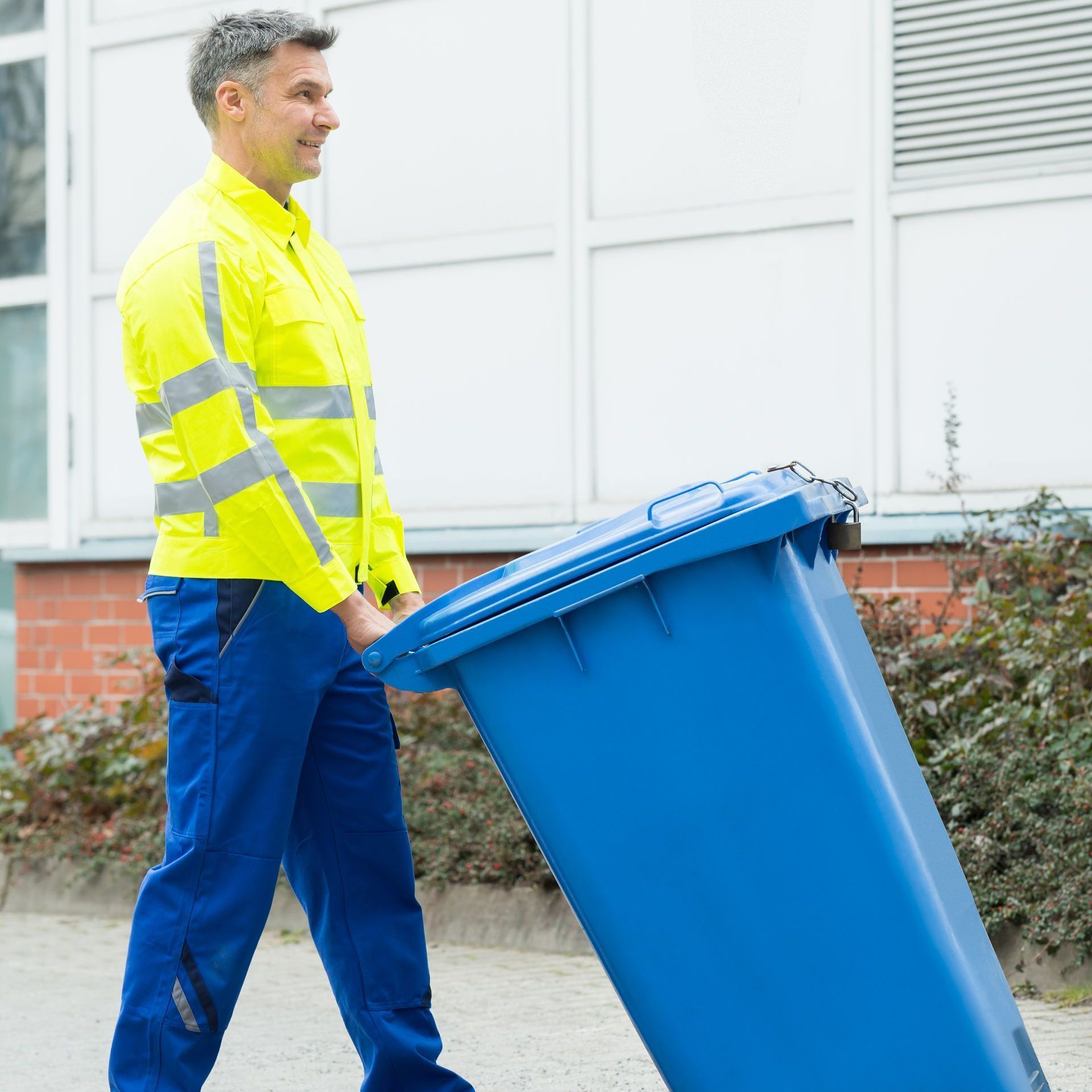 a man in a yellow jacket is pushing a blue trash can