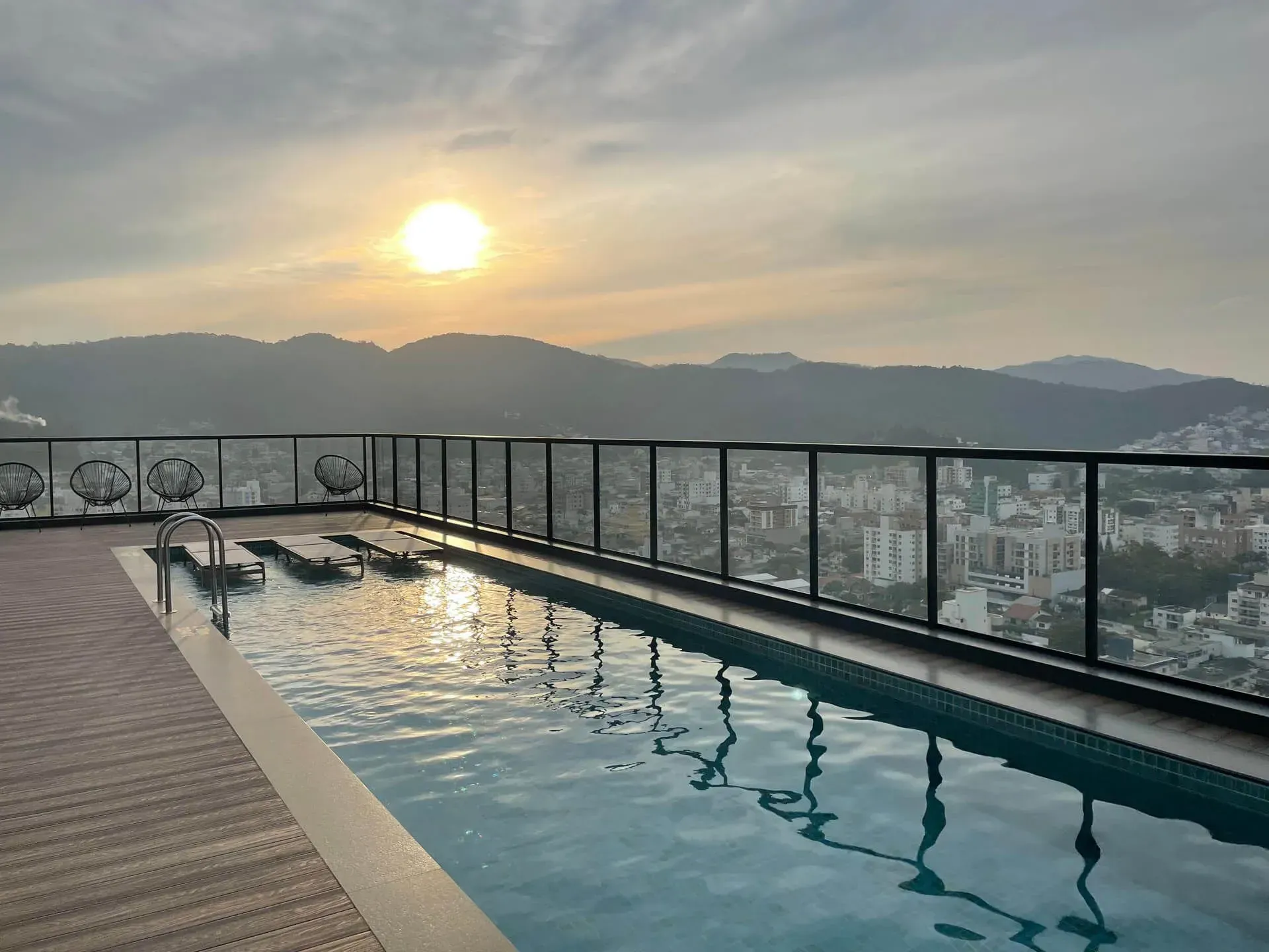 Uma grande piscina com vista para a cidade e as montanhas ao pôr do sol.