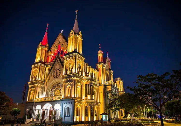 Uma grande igreja com uma torre vermelha é iluminada à noite.