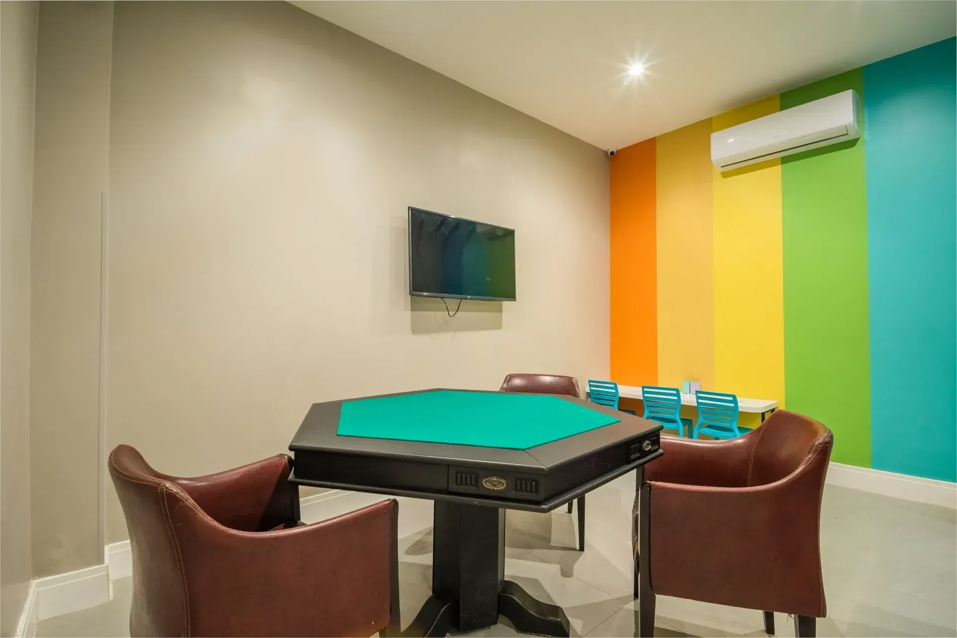 Uma sala de jogos com mesa e cadeiras e uma televisão na parede.