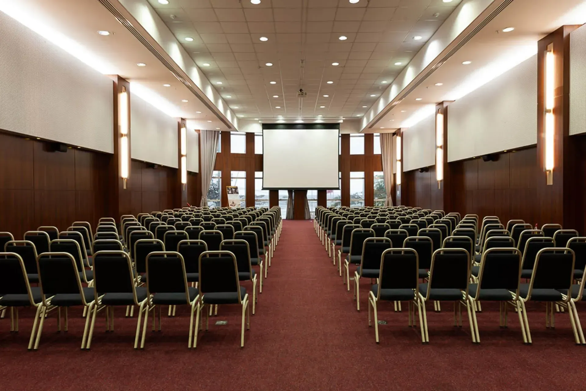 Uma sala de conferências vazia com fileiras de cadeiras e uma tela de projetor