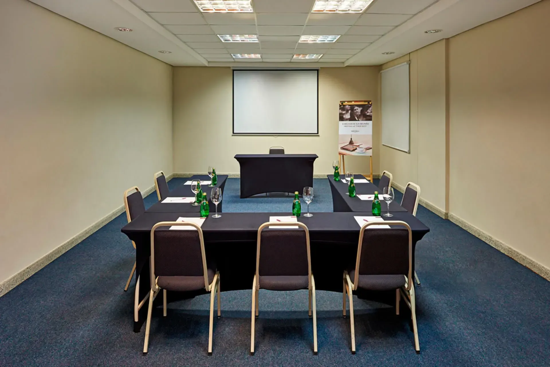Uma sala de conferências com mesas e cadeiras e uma tela de projetor