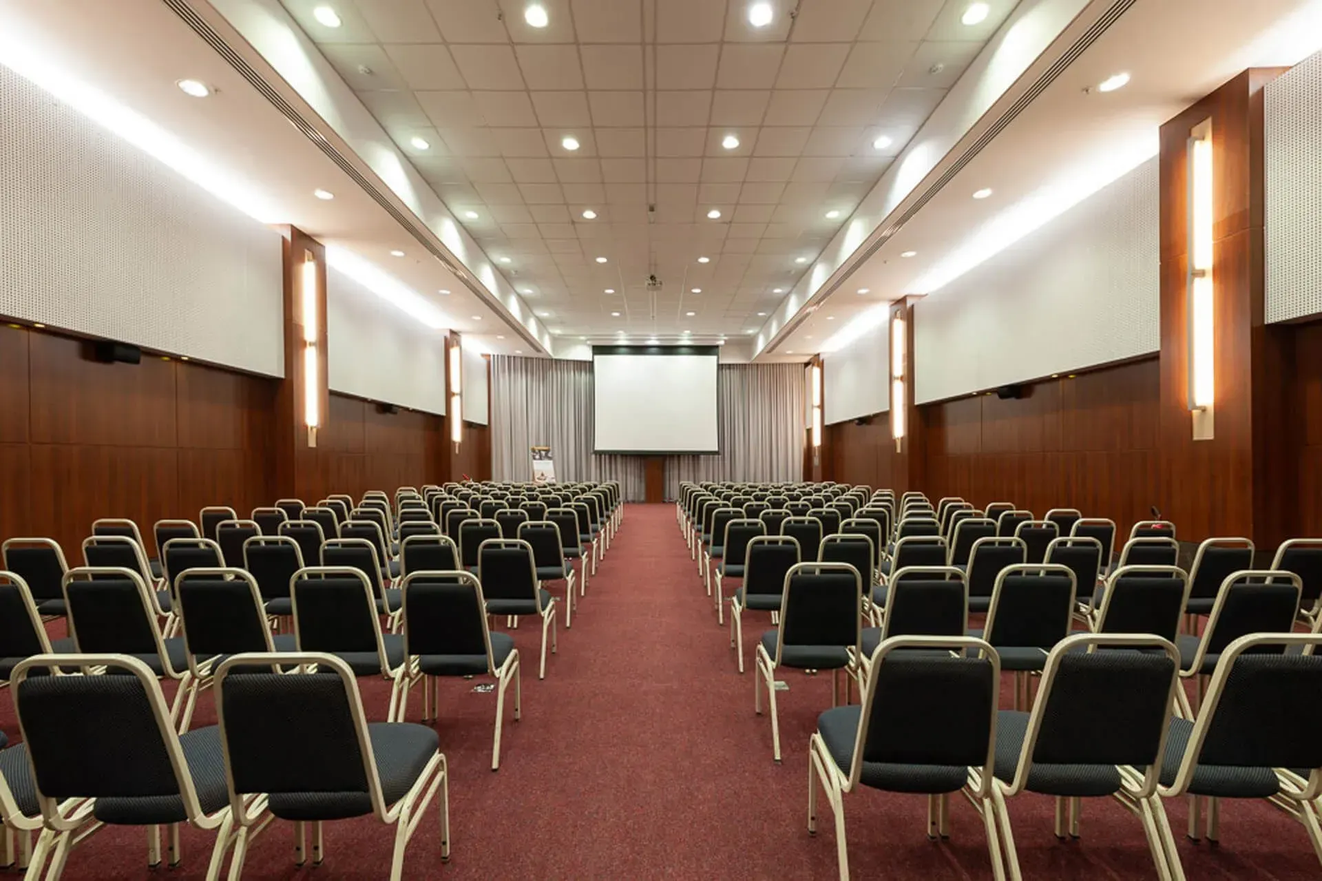 Um auditório vazio com fileiras de cadeiras e uma tela de projetor