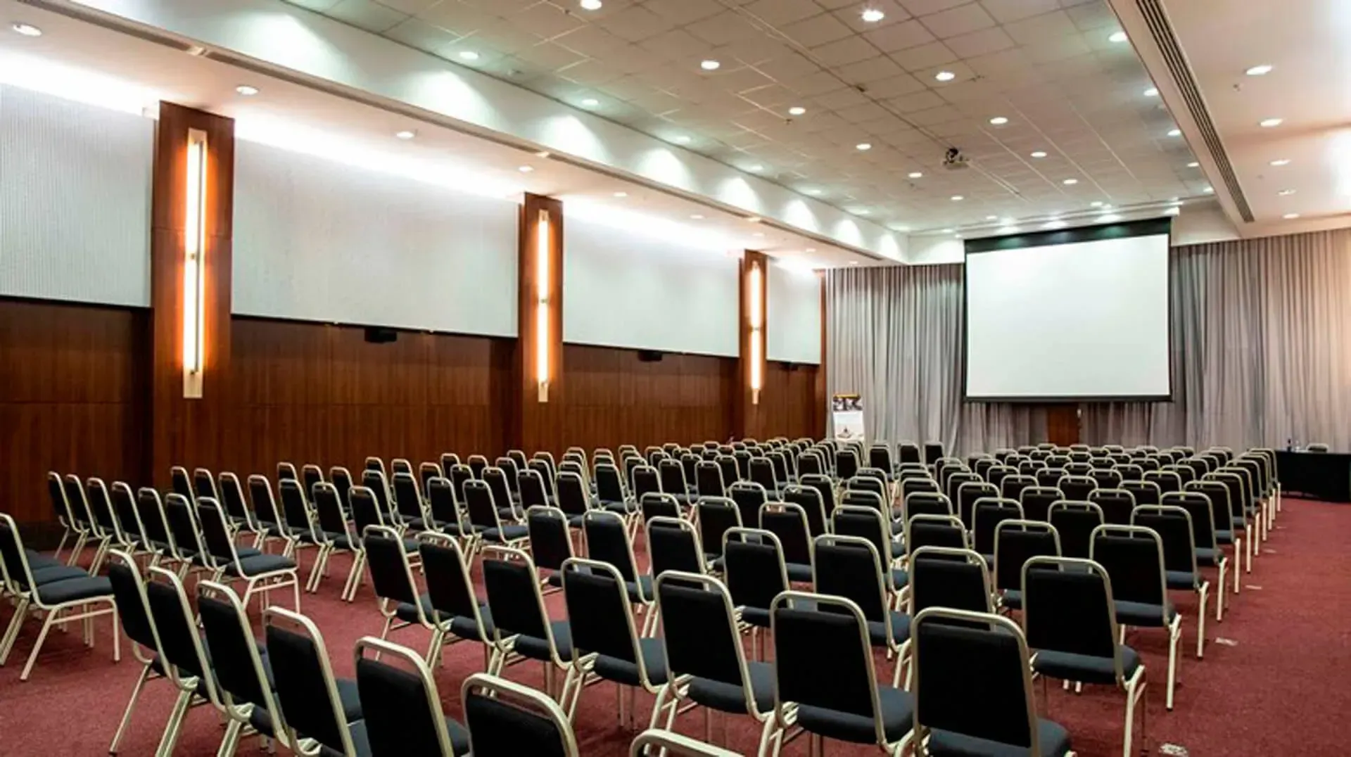 Uma sala grande com fileiras de cadeiras e uma tela de projetor