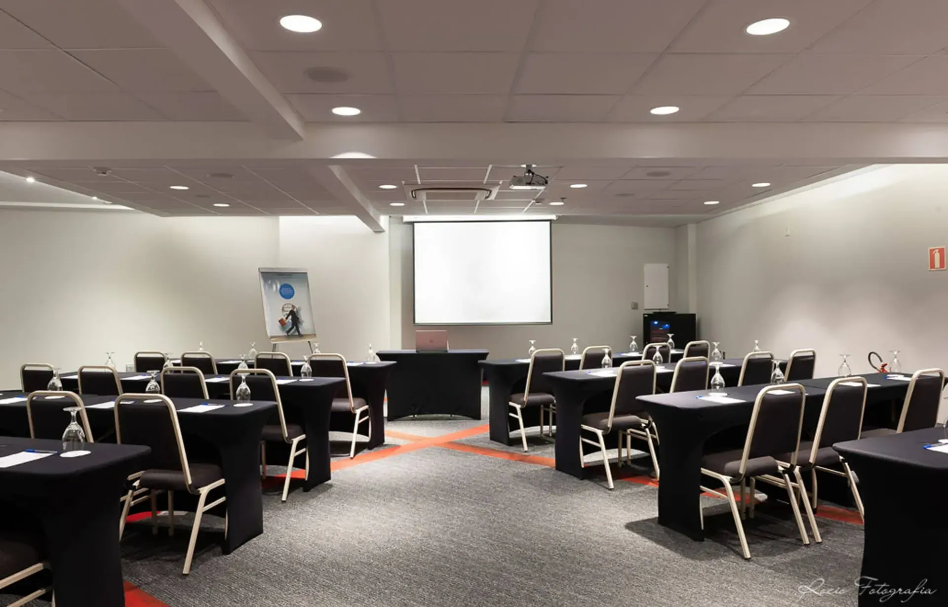Uma sala de conferências com mesas e cadeiras e uma tela de projetor
