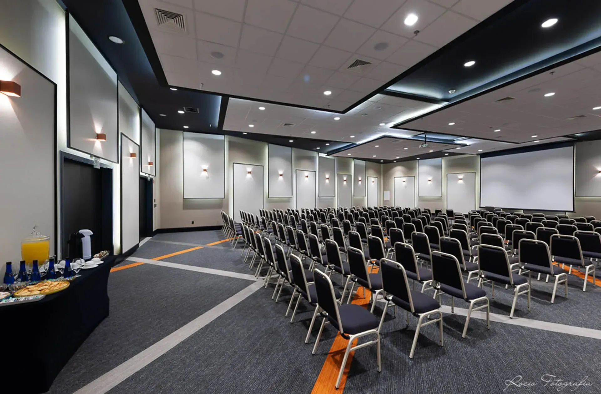 Uma grande sala de conferências com fileiras de cadeiras e uma tela de projetor