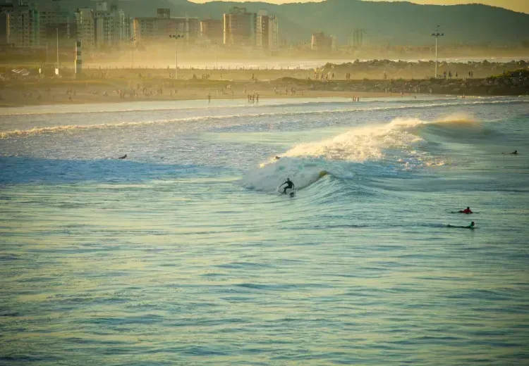 Um surfista está pegando uma onda no oceano com uma cidade ao fundo.