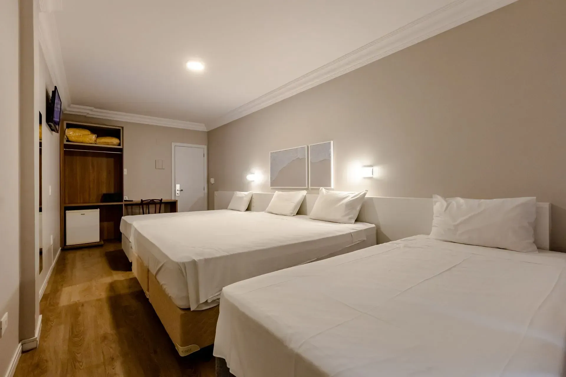 Um quarto de hotel com três camas e uma TV de tela plana.