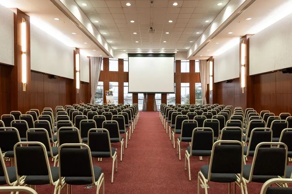 Uma grande sala de conferências com fileiras de cadeiras e uma tela de projetor