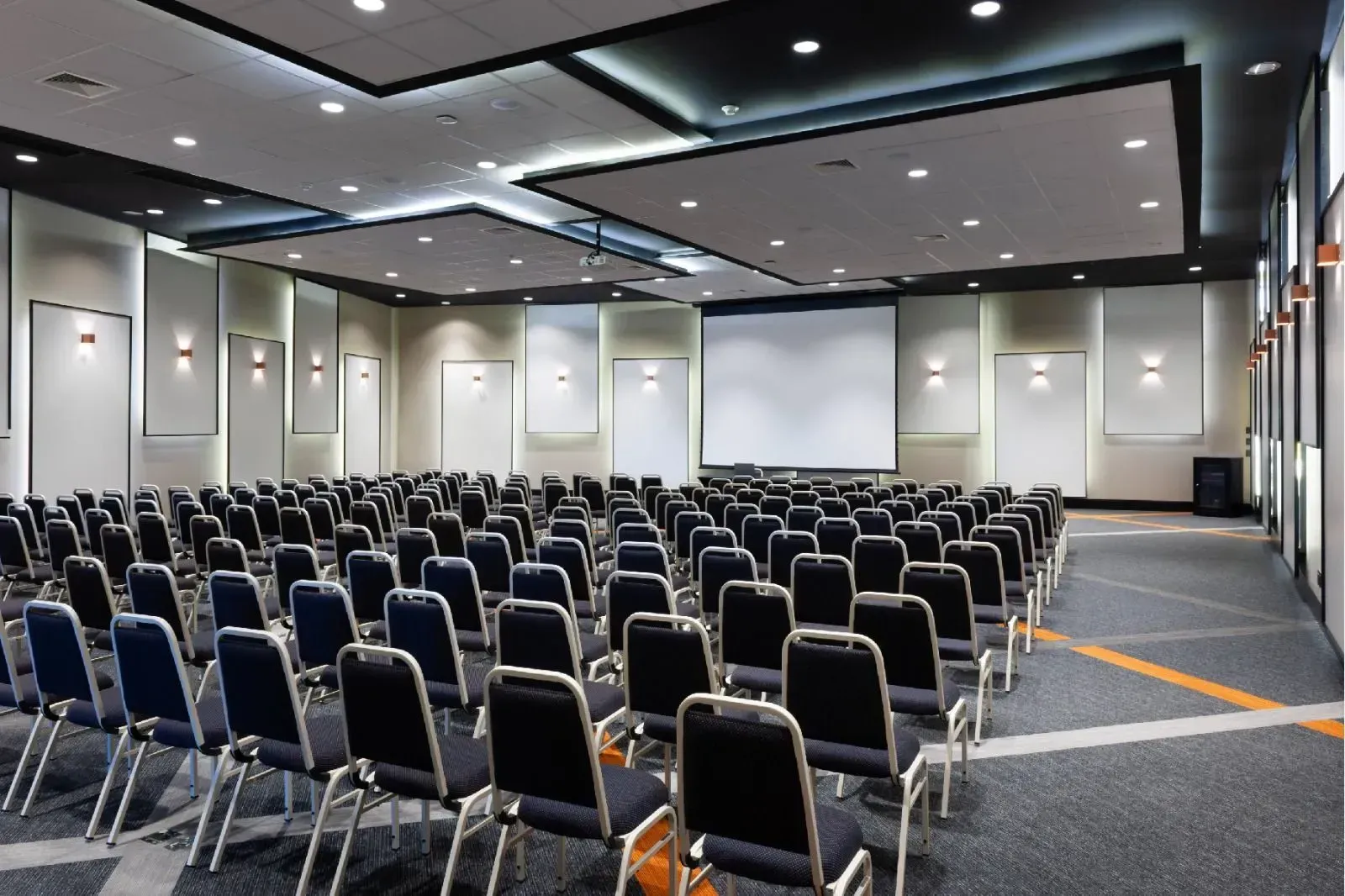 Uma grande sala de conferências com fileiras de cadeiras e uma tela de projetor