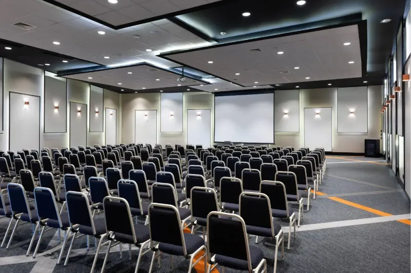 Uma grande sala de conferências com fileiras de cadeiras e uma tela de projetor