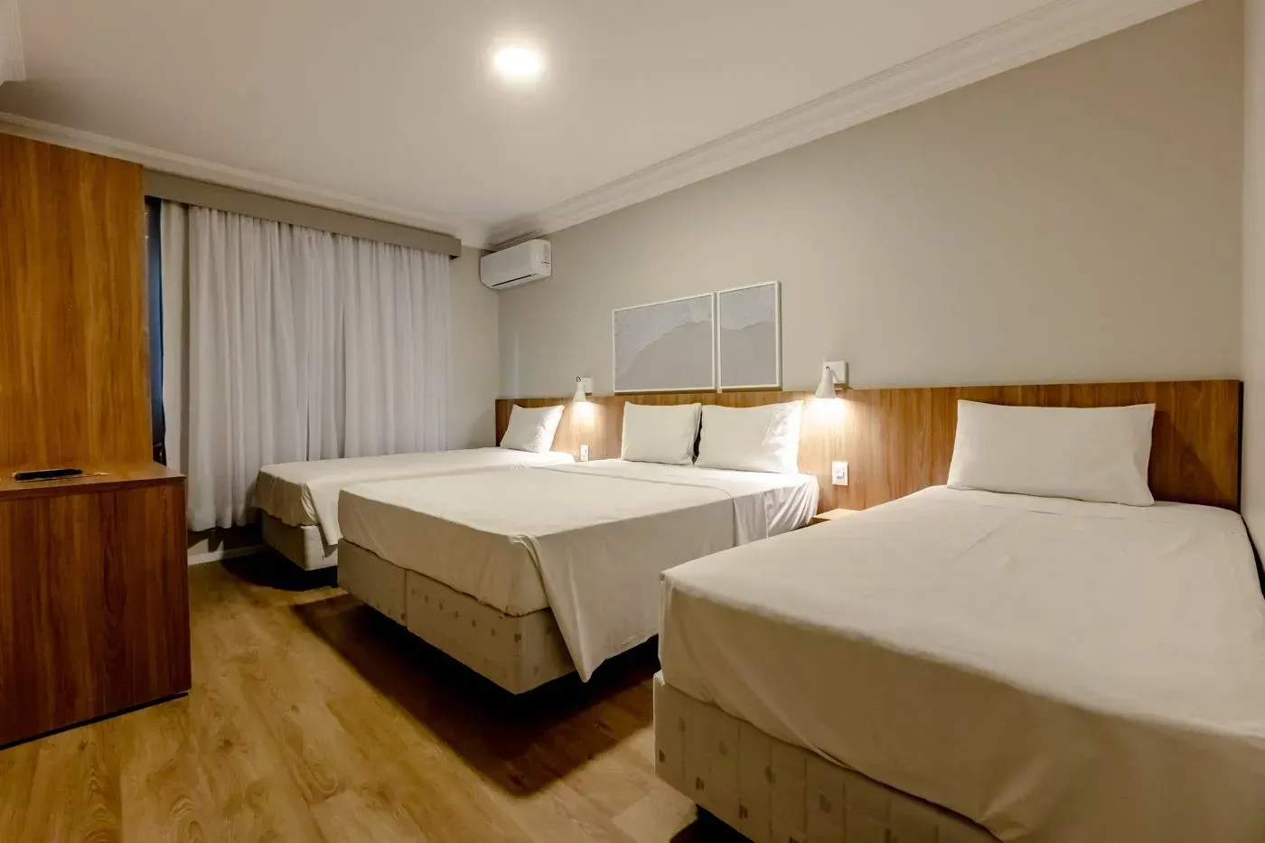 Um quarto de hotel com três camas e uma grande janela.