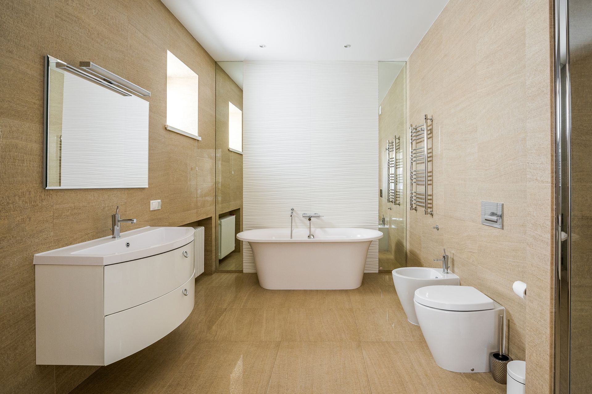 A modern, neutral-toned bathroom with a floating white vanity, freestanding tub, and wall-mounted toilet and bidet.