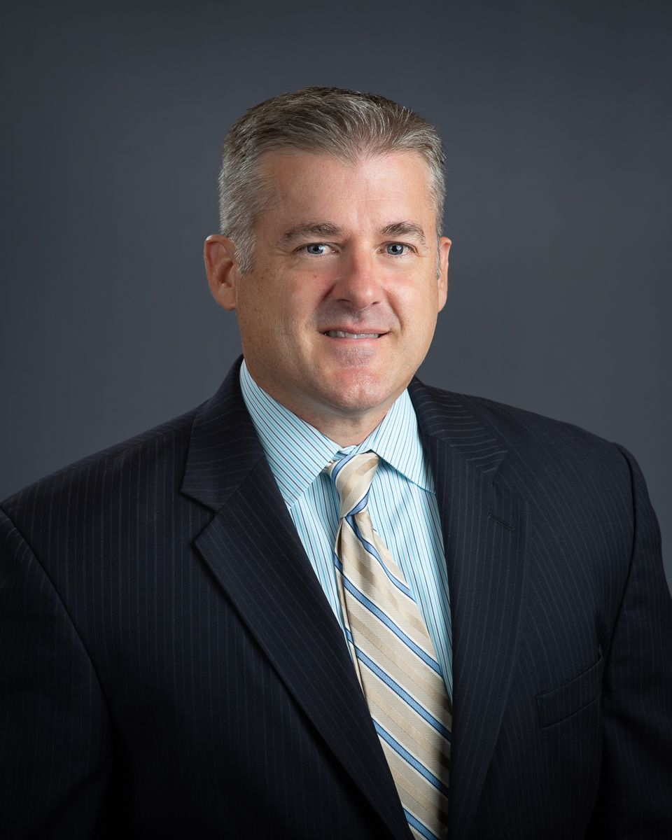 An elderly woman wearing a straw hat is standing in a greenhouse.