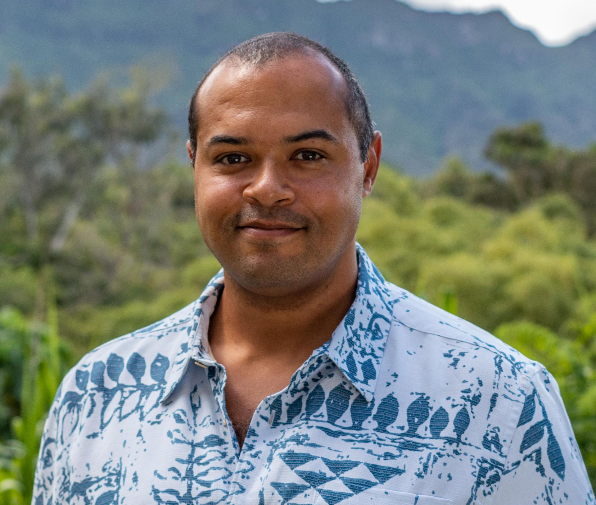 An elderly woman wearing a straw hat is standing in a greenhouse.