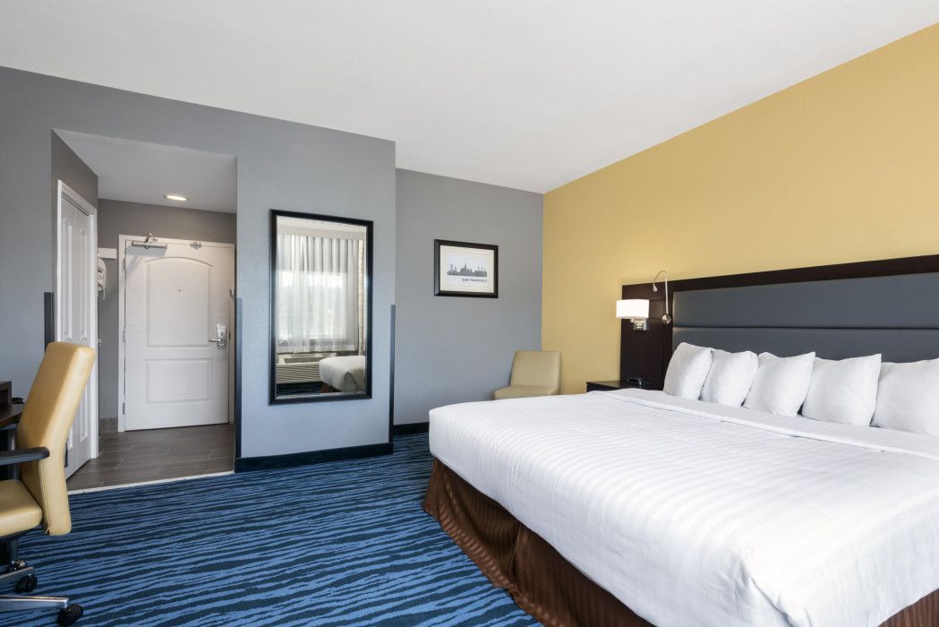 Hotel room with king-size bed, blue patterned carpet, gray walls, and yellow accent wall.