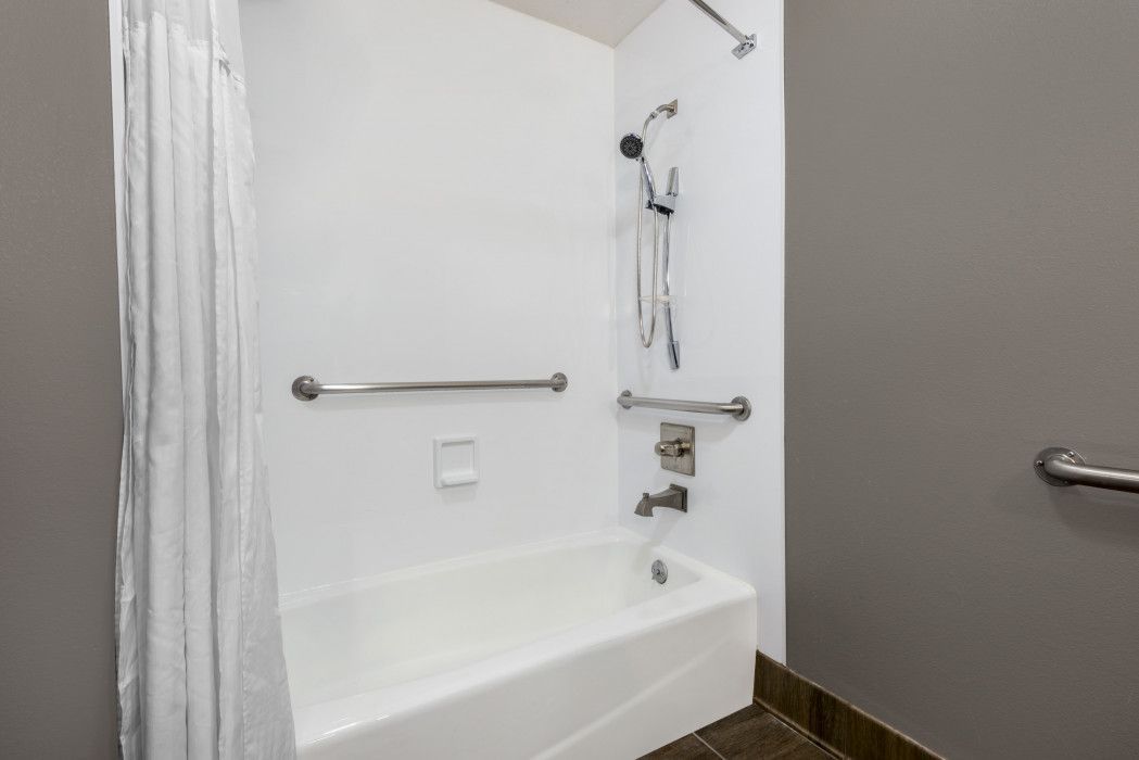 White accessible shower with grab bars and handheld shower head. Gray wall.
