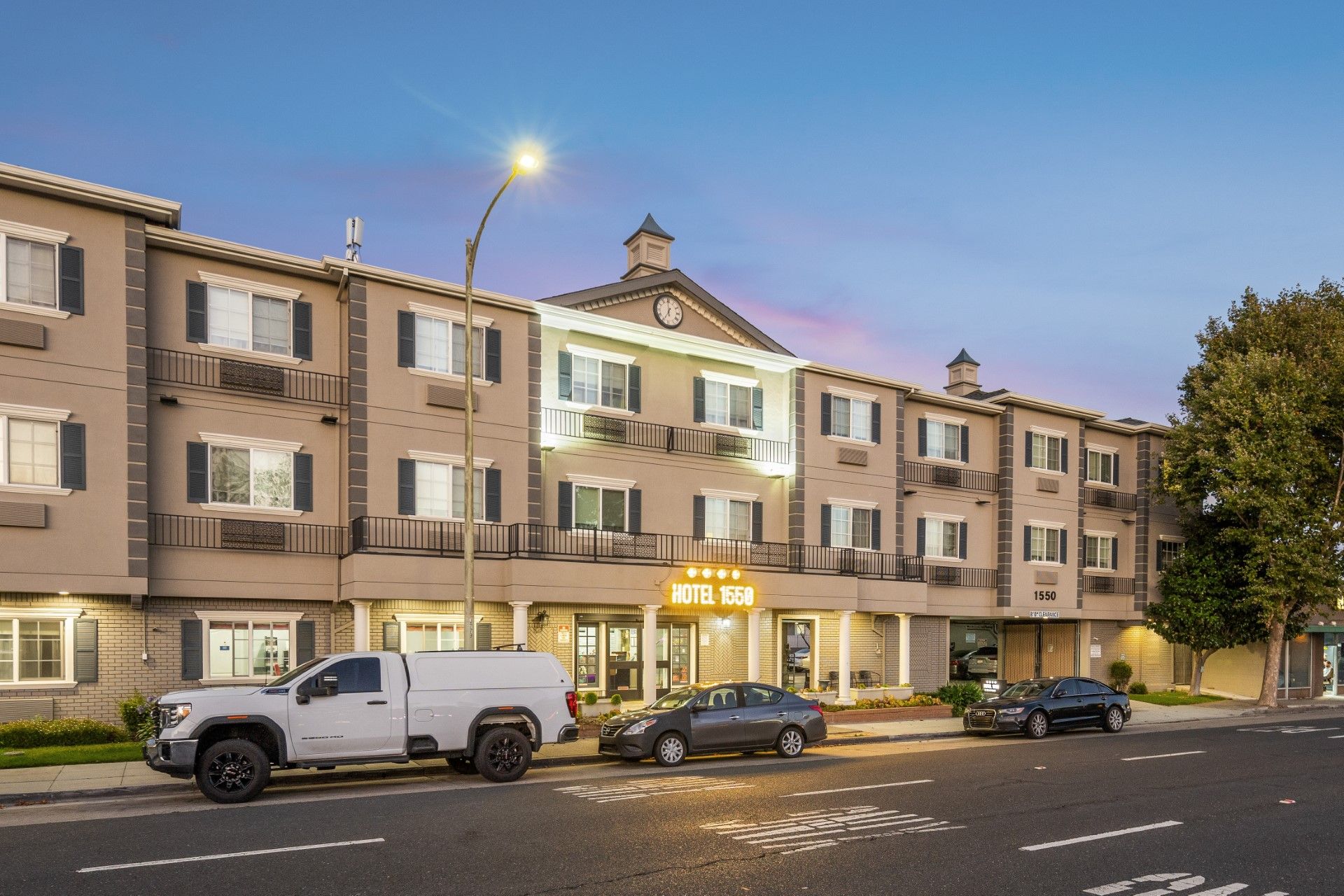 Hotel exterior at dusk with cars parked on street.