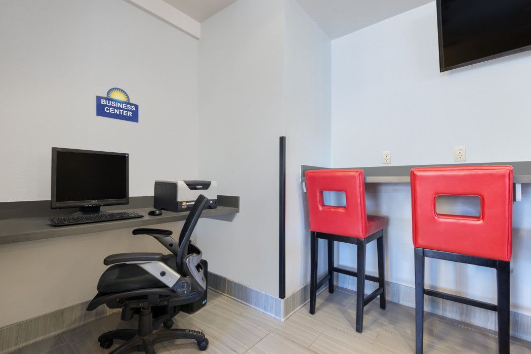 Computer desk and two red stools in a hotel business center; a computer and monitor sit at the desk.