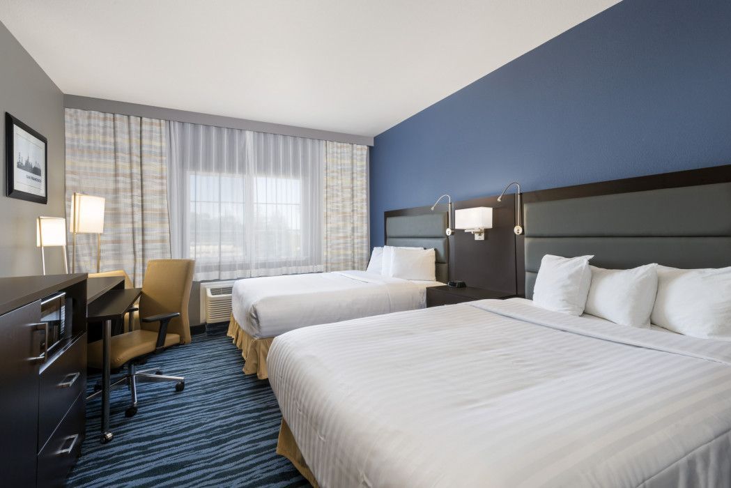 Hotel room with two beds, desk, and window with curtains; blue and white color scheme.