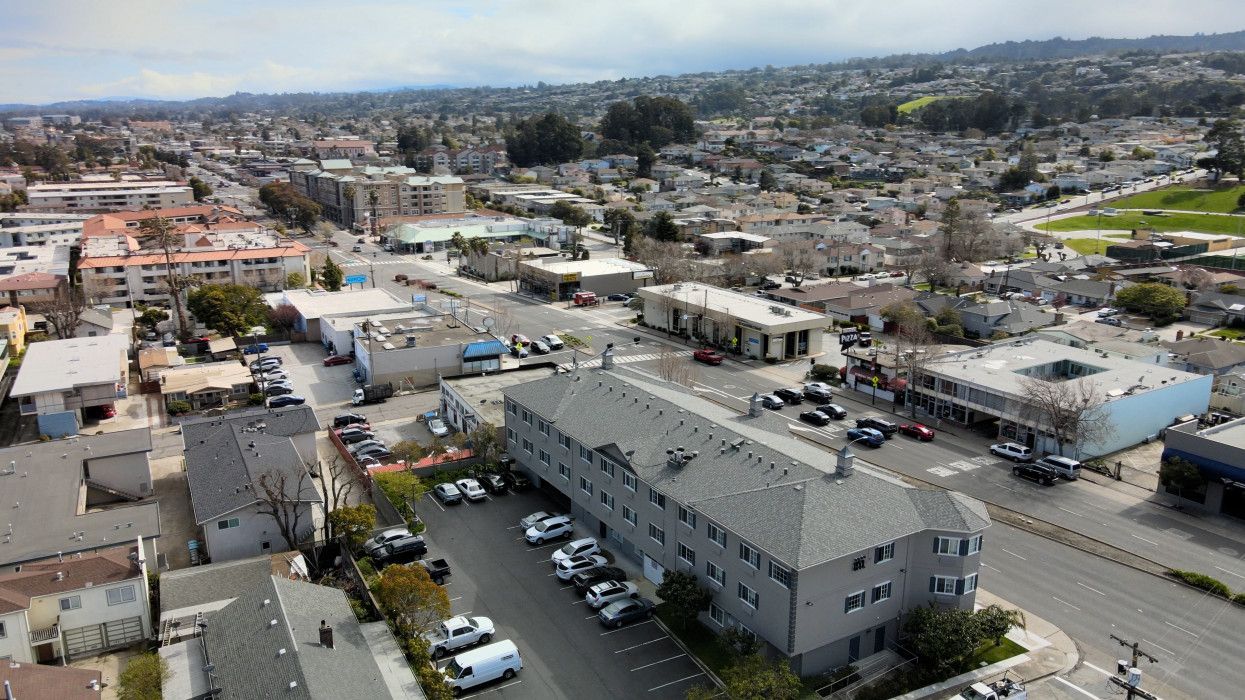 Aerial view of a town with buildings, parked cars, and a church steeple in the distance.