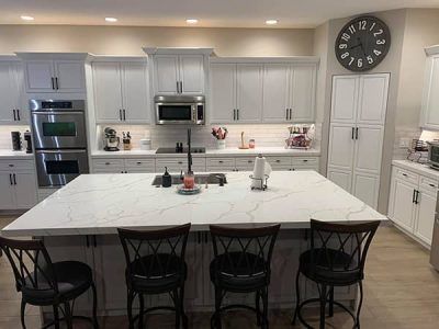 A kitchen with white cabinets , stainless steel appliances , a large island and a clock on the wall.