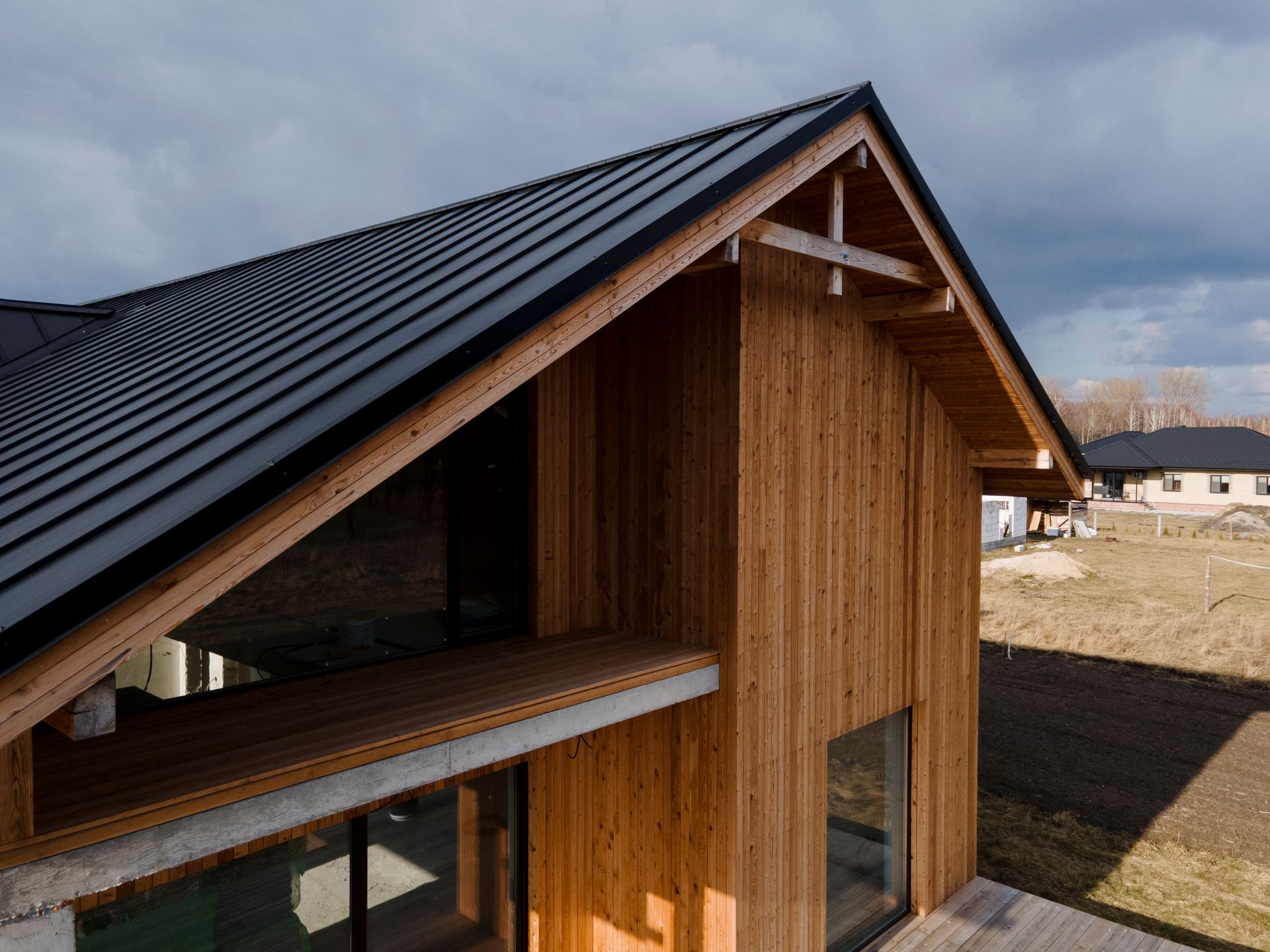 Wooden house with black metal roof under a cloudy sky.