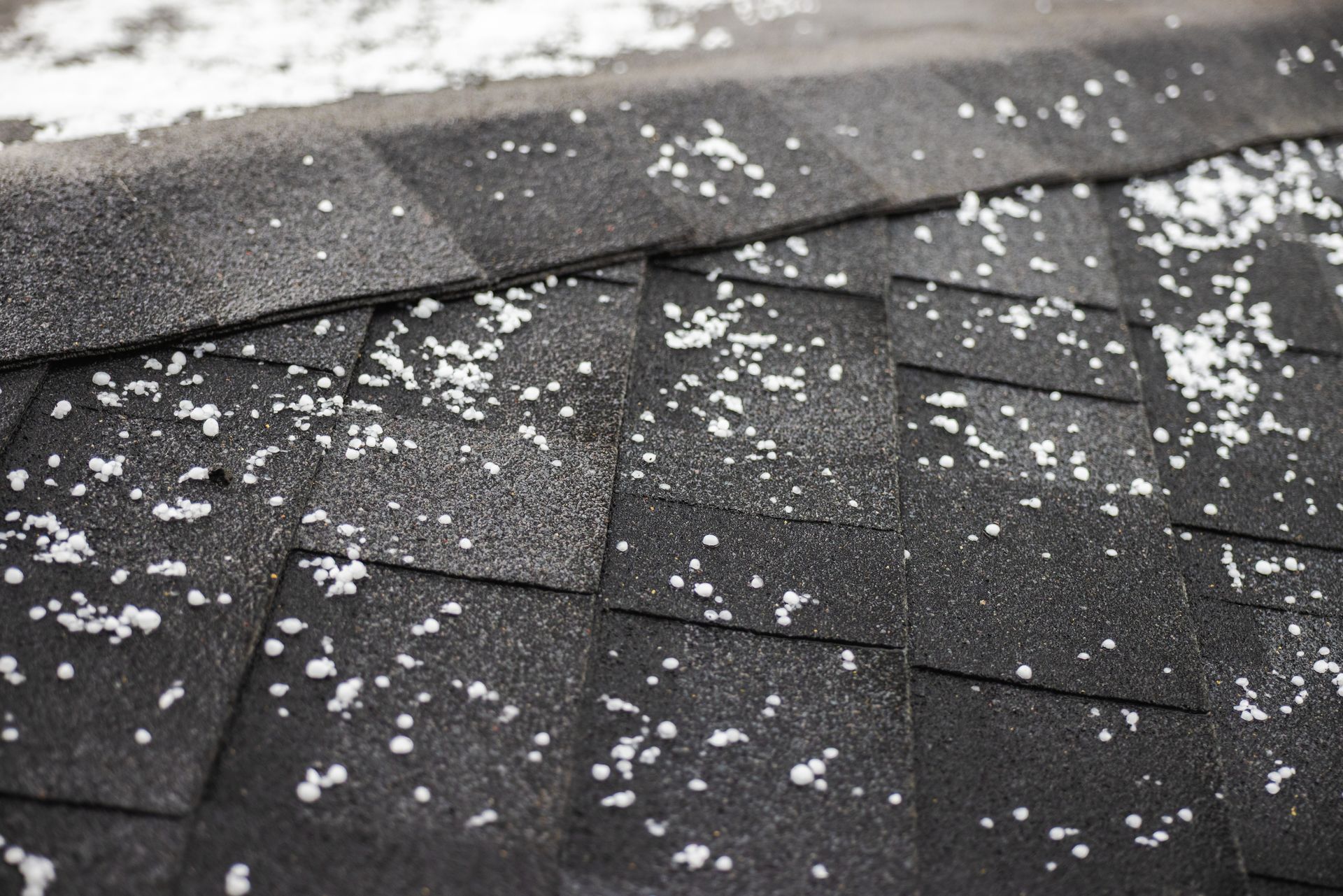 Black asphalt shingle roof covered in small hailstones.